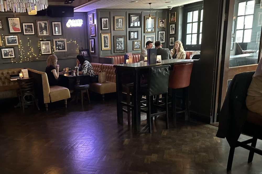 The interior of a traditional British pub with framed pictures and bar stools
